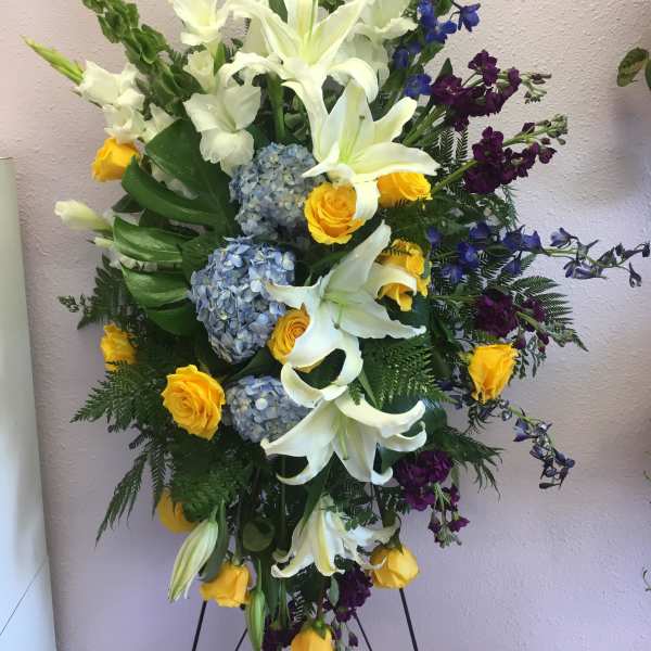 Tall floral spray with white lilies, yellow roses, blue hydrangeas, and purple accents