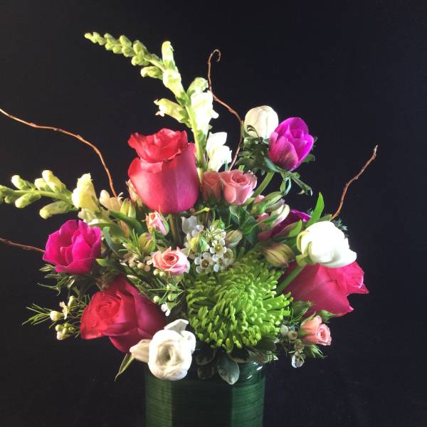Mixed bouquet of roses, snapdragons, and chrysanthemums in a green glass vase