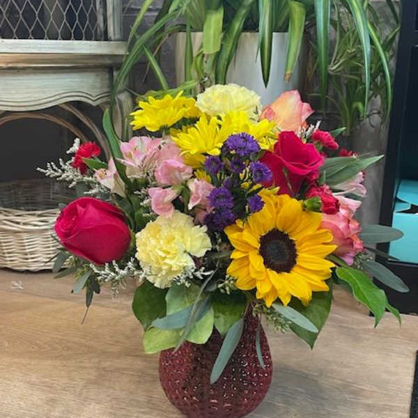 Mixed bouquet with sunflowers, roses, carnations, and alstroemeria in a red vase