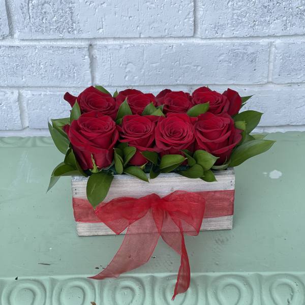 Red roses arranged in a wooden box with a red ribbon