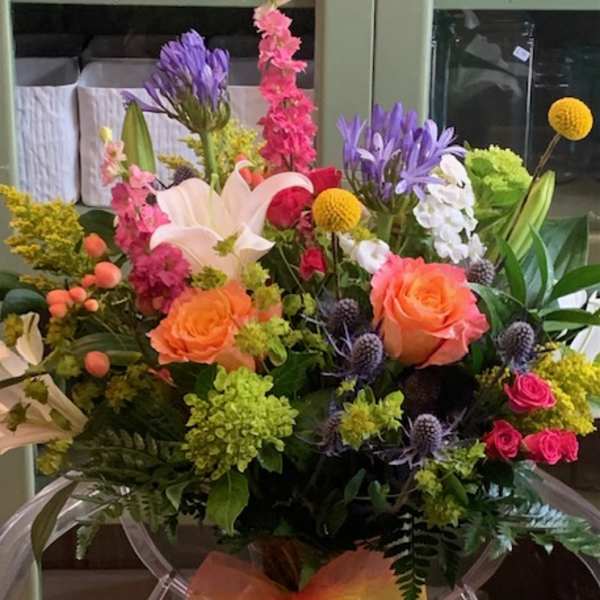 Bright mixed bouquet with orange roses, white lilies, and pink blooms in a clear vase with an orange bow