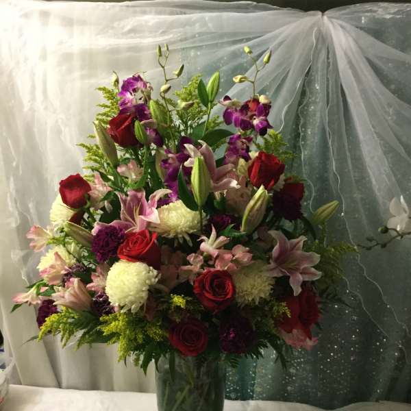Tall bouquet of red roses, pink lilies, and purple orchids in a glass vase