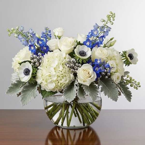 White roses and blue flowers in a clear glass bowl vase