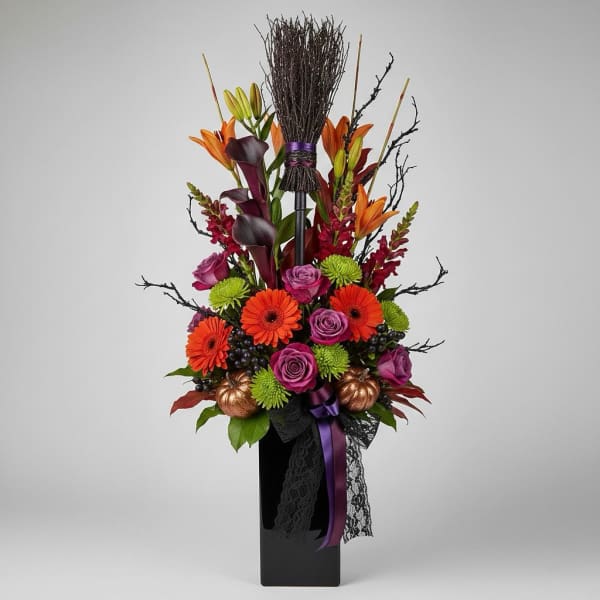 Tall floral arrangement with orange lilies, purple roses, and gerbera daisies in a black vase