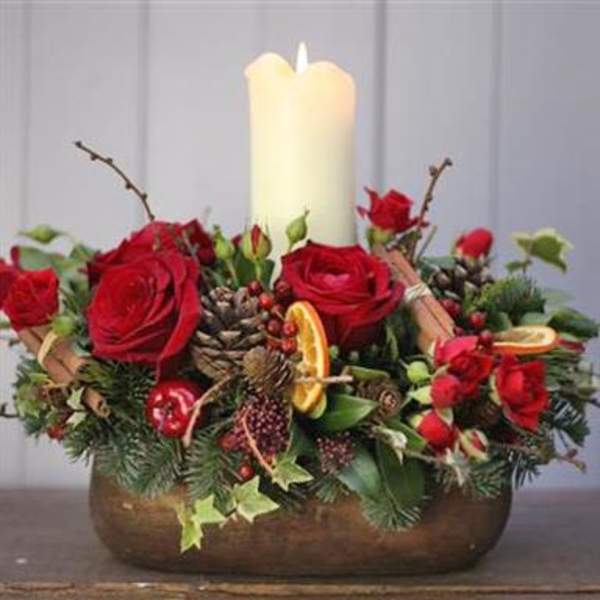 Red roses arranged around a white pillar candle in a low container