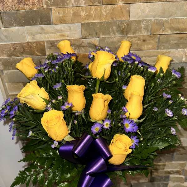 Yellow roses and purple daisies in a glass vase with a purple ribbon