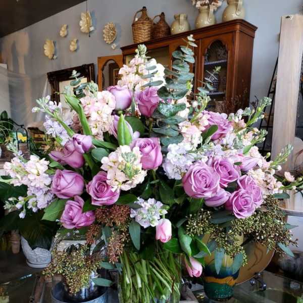 Lavender roses and pale pink flowers arranged in a clear glass vase