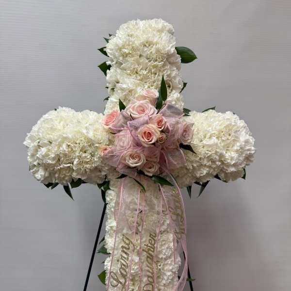 White floral cross with pink roses and ribbon on a stand