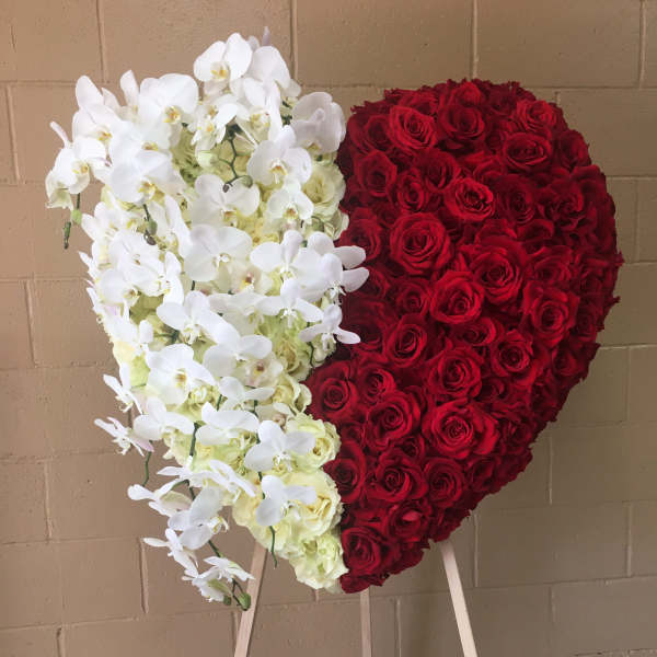 Heart-shaped floral display of red roses and white orchids on an easel