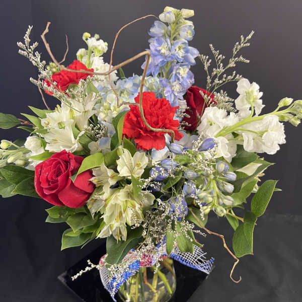Mixed bouquet of red roses, white lilies, and blue flowers in a glass vase