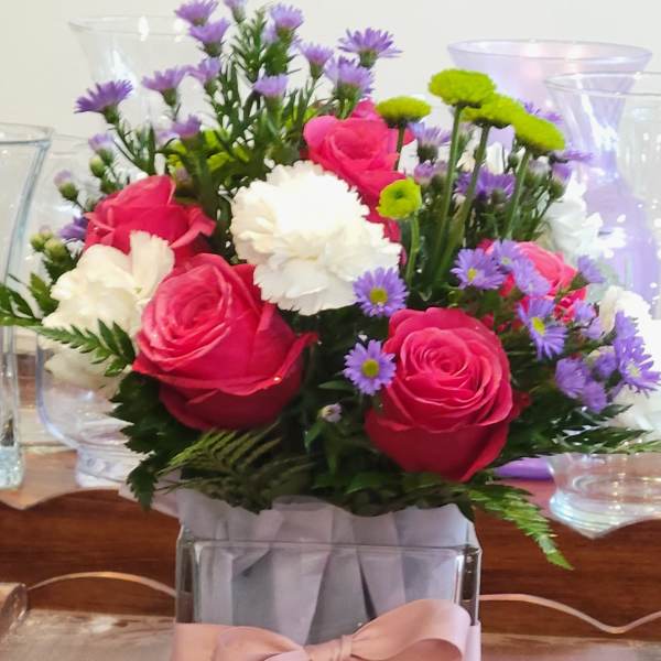Pink roses and white carnations in a square glass vase with a pink ribbon