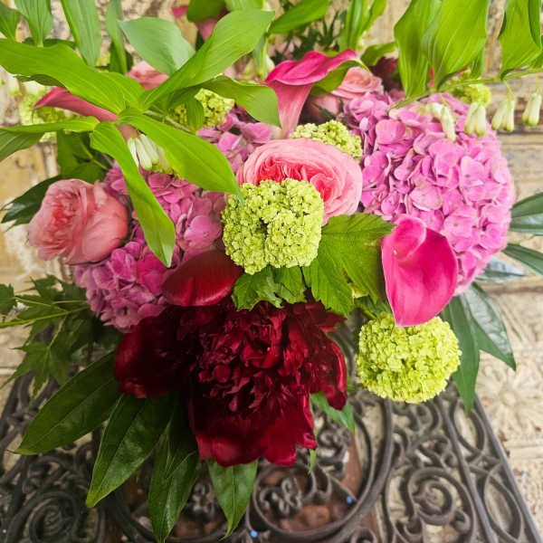 Pink and burgundy floral arrangement with green blooms and tropical leaves