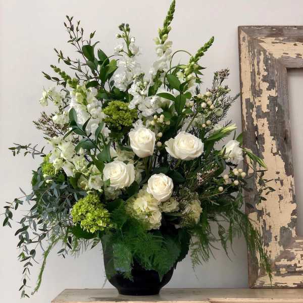 Tall arrangement of white roses, white snapdragons, and green hydrangeas in a black vase
