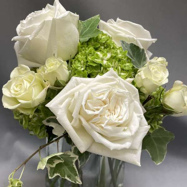 Small white rose and green hydrangea arrangement in a clear glass vase