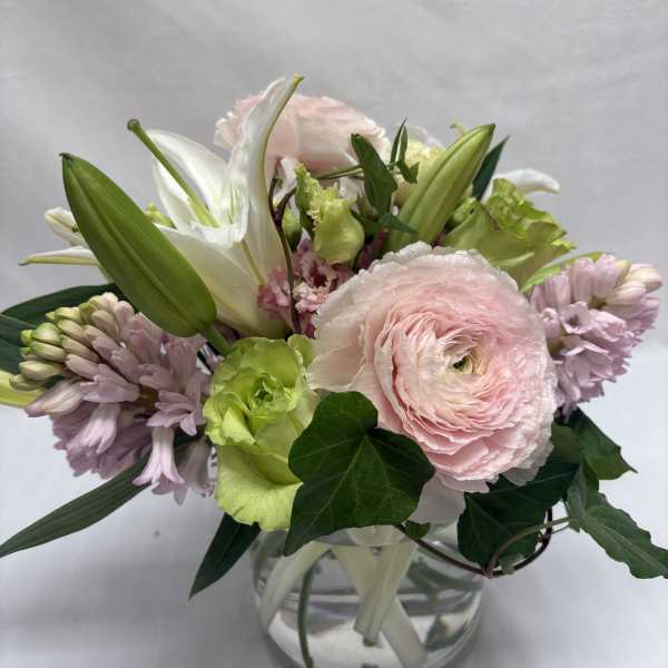 Pastel bouquet of pink ranunculus, lilies, and hyacinths in a round glass vase