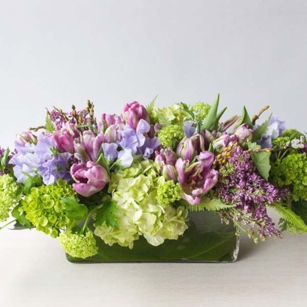 Low floral arrangement with purple, pink, white, and green blooms in a rectangular vase