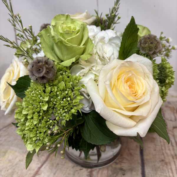 Low arrangement of cream roses, green blooms, and white hydrangeas in a clear glass vase