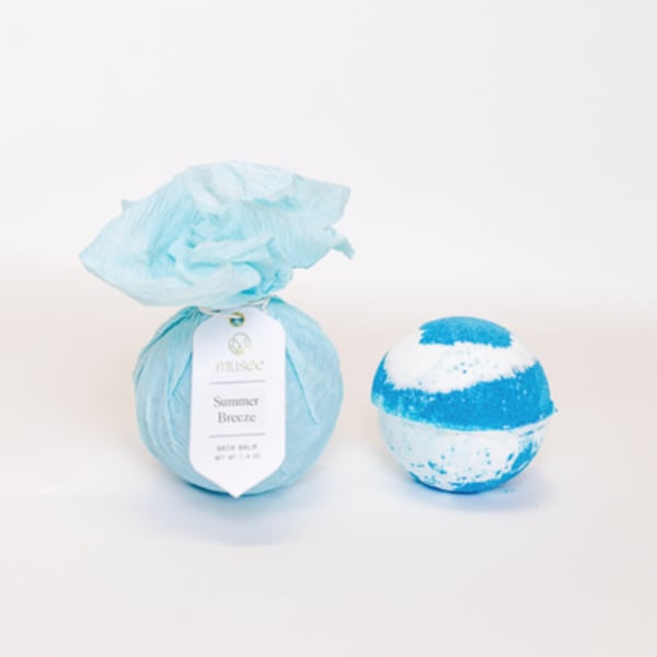 Blue bath bomb wrapped in tissue paper beside a striped bath bomb