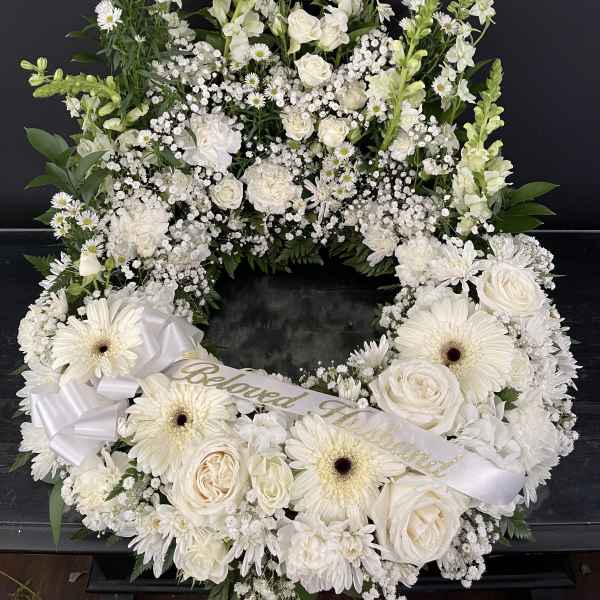 White floral funeral wreath with roses, daisies, and ribbon