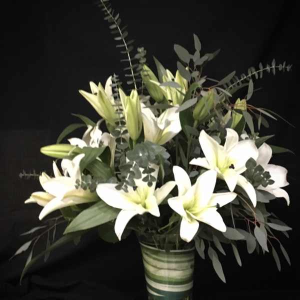 White lilies arranged in a clear glass vase with eucalyptus foliage