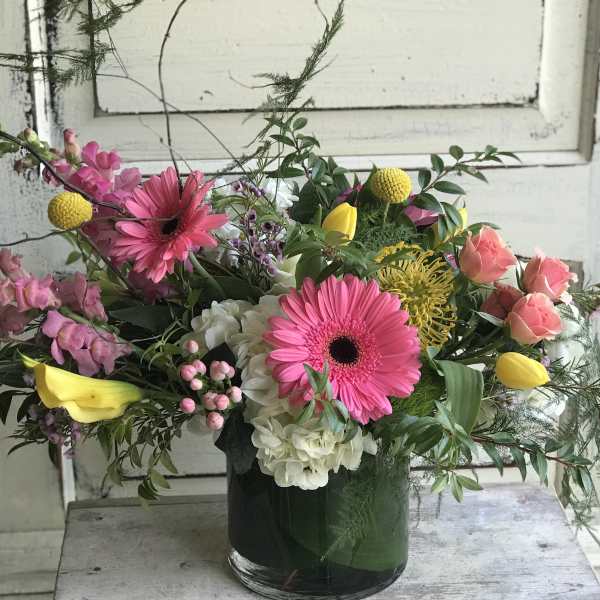 Mixed bouquet in a glass vase with pink gerberas, yellow tulips, and roses