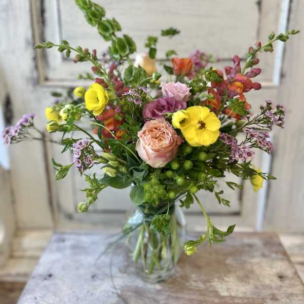 Mixed bouquet of yellow, pink, and purple flowers in a clear glass vase