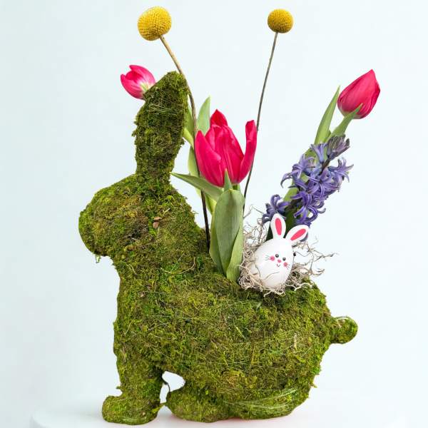 Moss-covered bunny-shaped floral display with pink tulips, purple hyacinth, and a small bunny egg