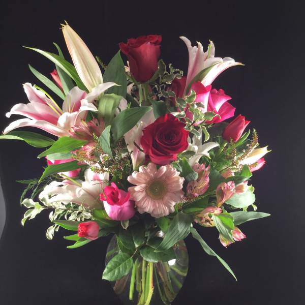 Mixed bouquet of red roses, lilies, and pink daisies in a glass vase