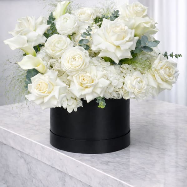 White roses and calla lilies arranged in a black round box