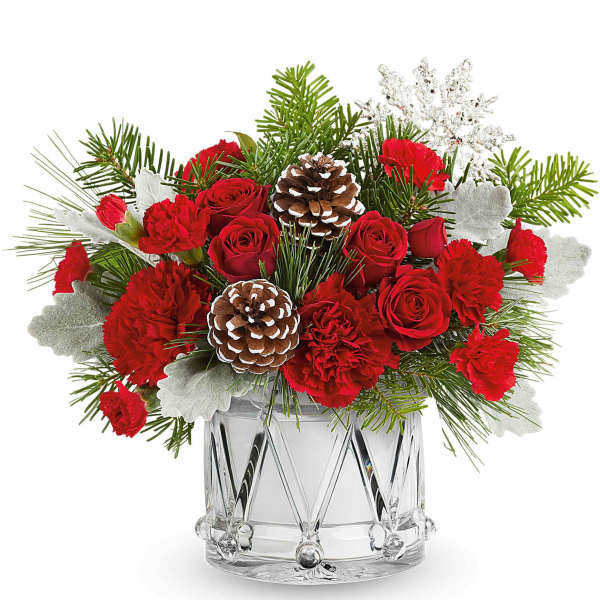 Red roses and carnations in a clear glass vase with pinecones and winter greenery