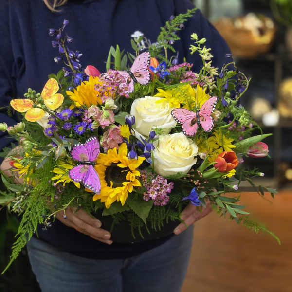 Colorful mixed flower arrangement in a black container with butterfly picks