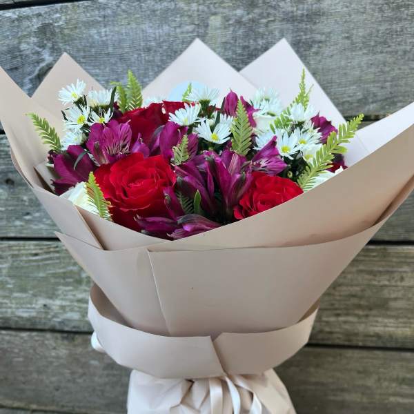 Bouquet of red roses, purple blooms, and white daisies wrapped in beige paper