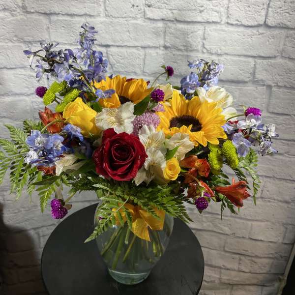 Mixed bouquet with sunflowers, roses, and blue flowers in a glass vase