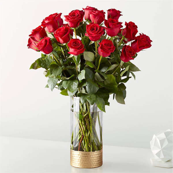 Red roses arranged in a clear glass vase with a gold base