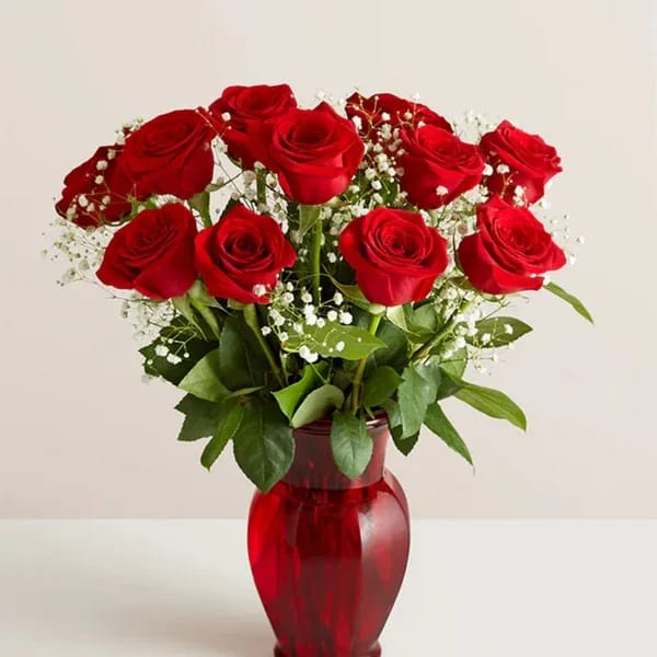 Red roses arranged in a red glass vase with white baby's breath