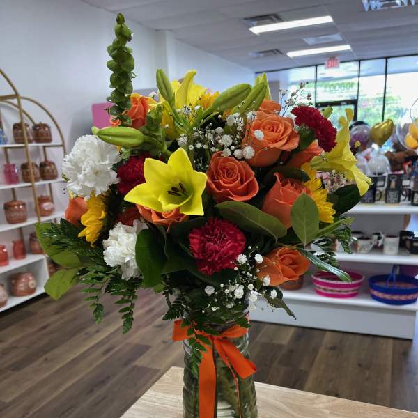 Mixed bouquet of orange roses, yellow lilies, and white carnations in a glass vase
