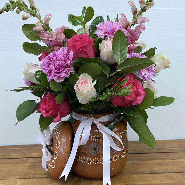 Pink roses and carnations arranged in a painted ceramic pitcher with ribbon