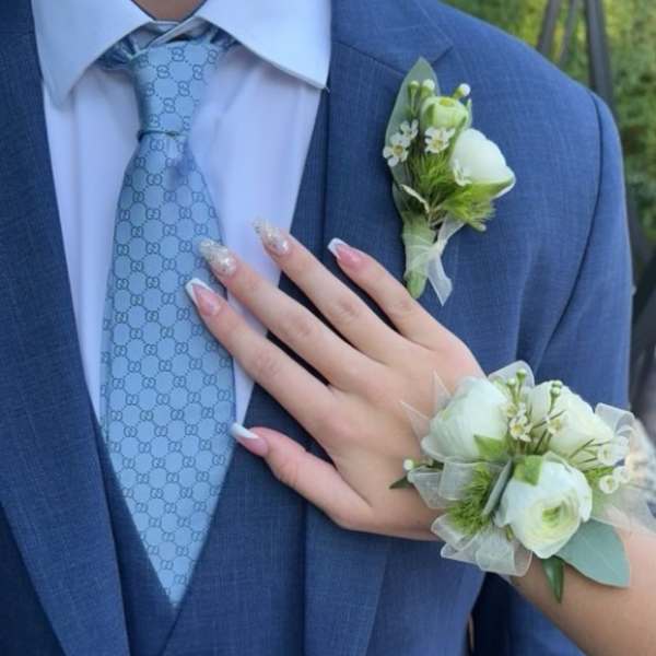 White floral wrist corsage and matching boutonniere worn with a blue suit