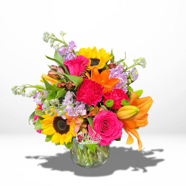 Bright mixed bouquet in a glass vase with sunflowers, roses, lilies, and carnations