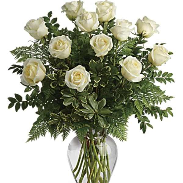 White roses arranged in a clear glass vase with greenery