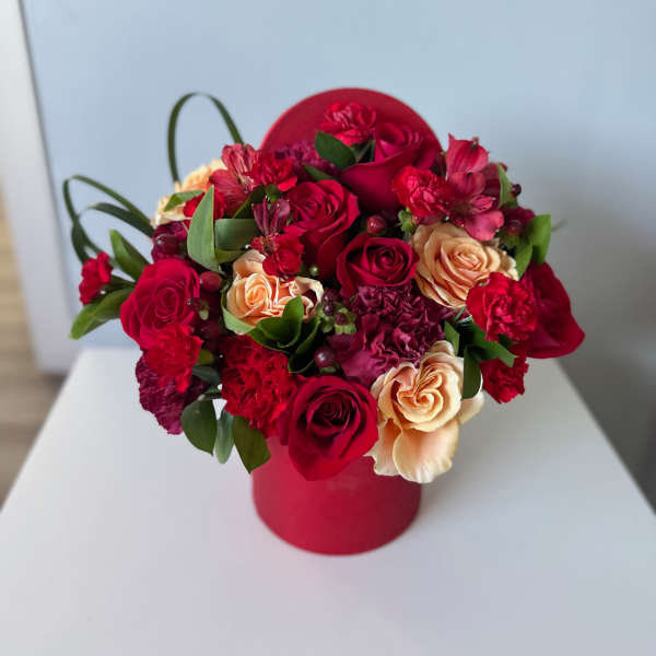 Red and peach roses arranged in a round red box