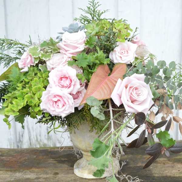 Pink roses and mixed greenery arranged in a stone vase