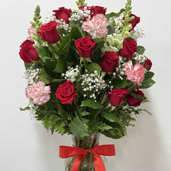 Red roses and pink carnations in a glass vase with a red ribbon
