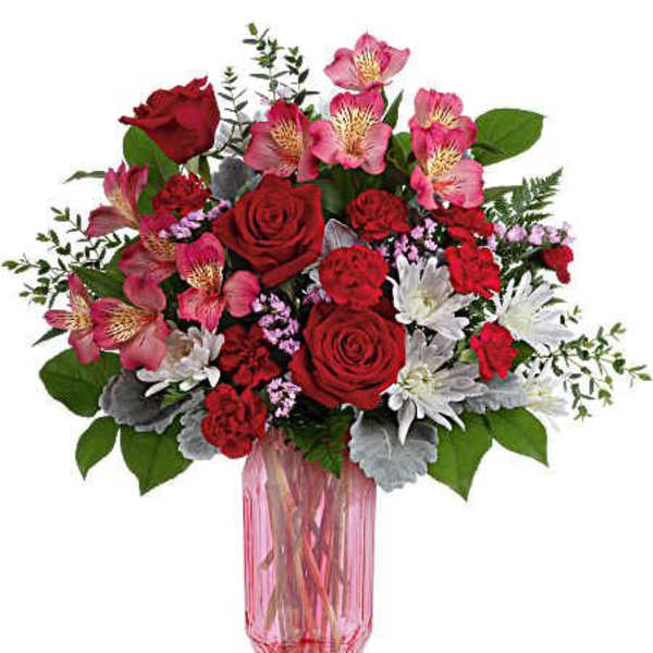 Bouquet of red roses, pink alstroemeria, and white daisies in a pink glass vase