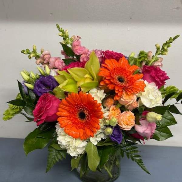 Mixed bouquet with orange gerbera daisies and pink, purple, and white flowers in a glass vase