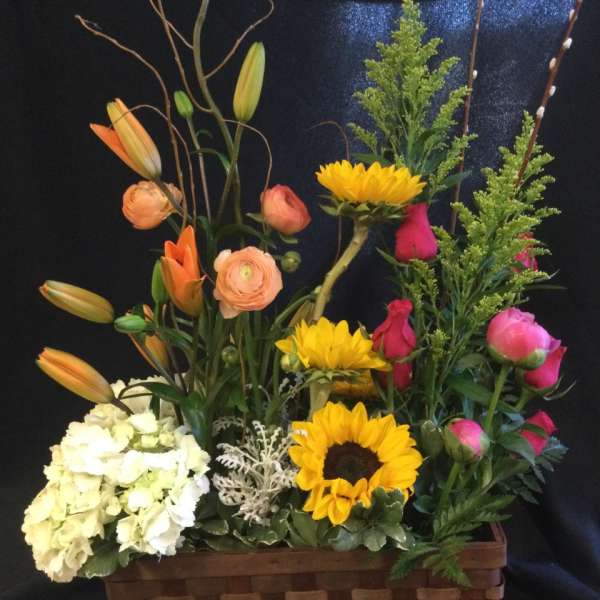 Mixed flower arrangement in a woven basket with lilies, roses, sunflowers, and hydrangea