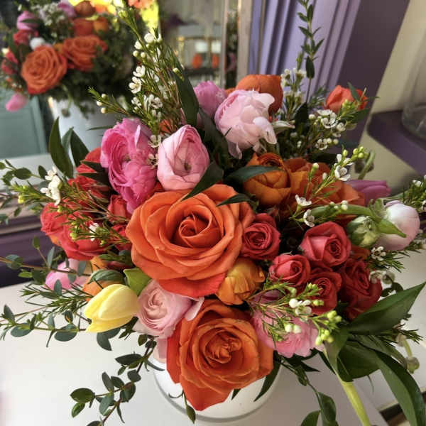 Mixed bouquet of orange, pink, and red roses in a white vase