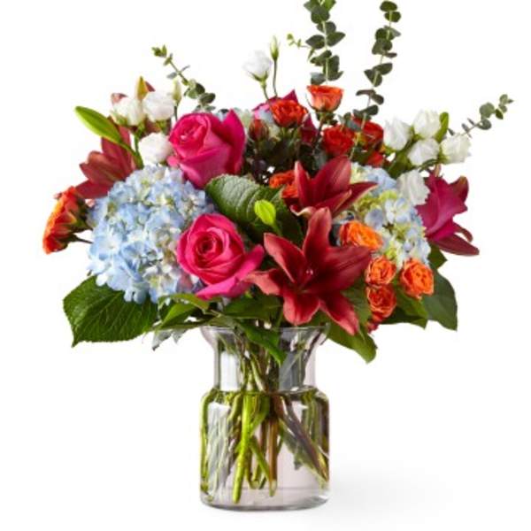 Mixed bouquet of pink roses, lilies, hydrangeas, and white blooms in a glass vase