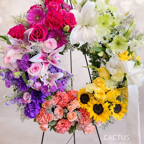 Colorful floral wreath on a black stand with roses, lilies, and sunflowers