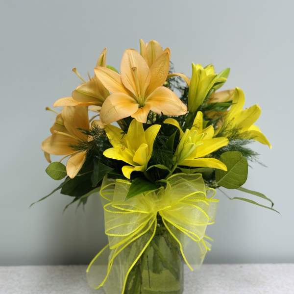 Yellow and peach lilies arranged in a glass vase with a ribbon bow.